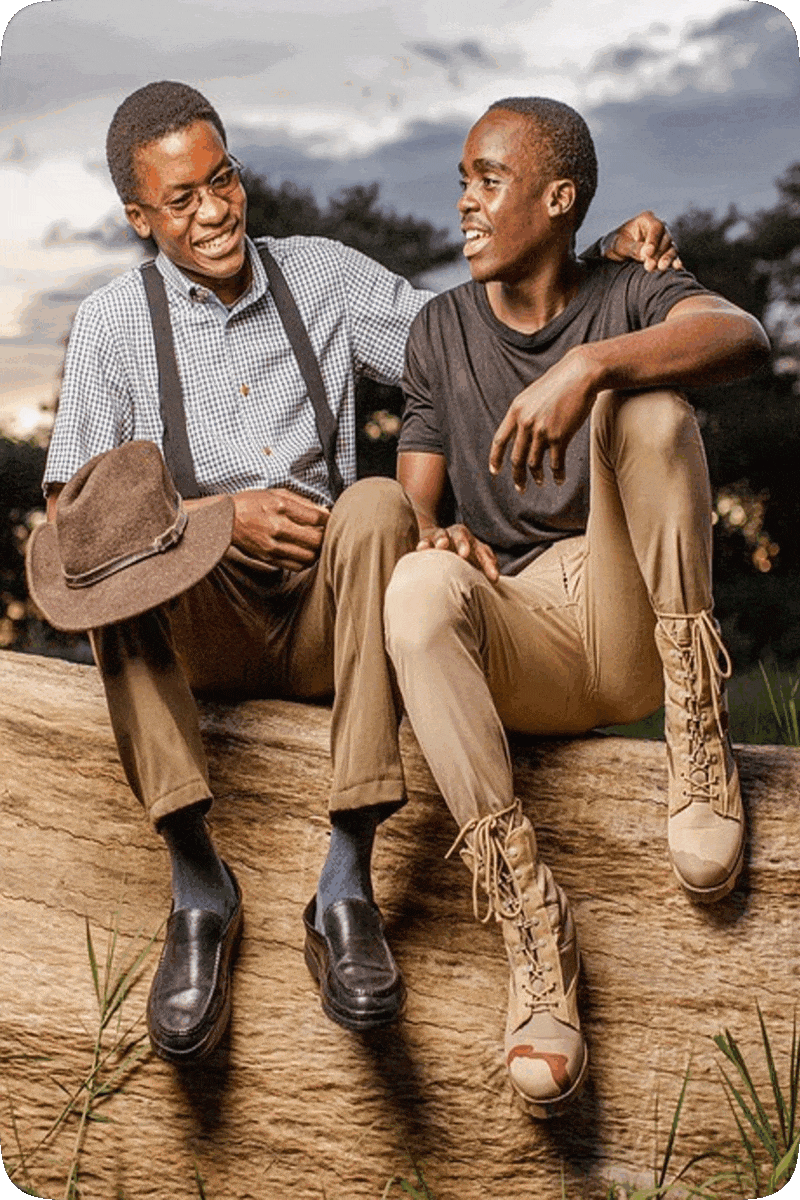 Picture of two happy smiling men sitting outside on a large rock.