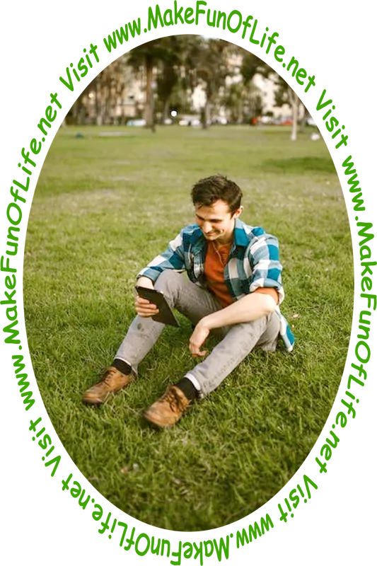 Picture of a man sitting on the ground in a green grassy area and looking at a tablet computer.