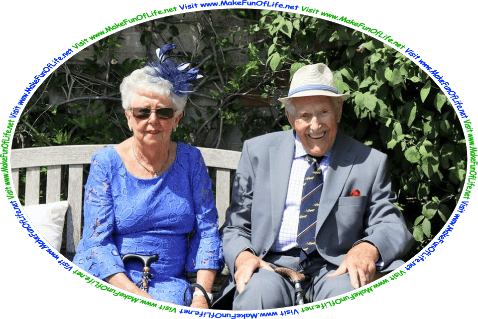 Picture of a happy, smiling older married couple outside on a bright, sunny day, seated on a wooden bench with a brick wall covered in green leafy plants behind them, and the words, ‘Visit www.MakeFunOfLife.net.’