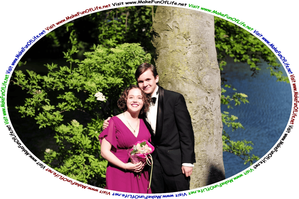 Picture of a happy smiling couple on their wedding day standing under a green leafy Tree next to a calm blue lake, and the words, ‘Visit www.MakeFunOfLife.net.’