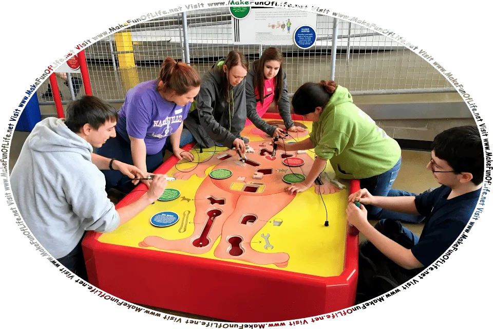 Picture of six young people playing the Operation Game from toymaker Hasbro. Players exercise manual dexterity by using tweezers connected to wires to remove various items from the patient. The object of the game is to remove the items without touching the sides of the openings. Physical contact between the sides of the openings in which the items are located and the tweezers triggers a loud buzzer.